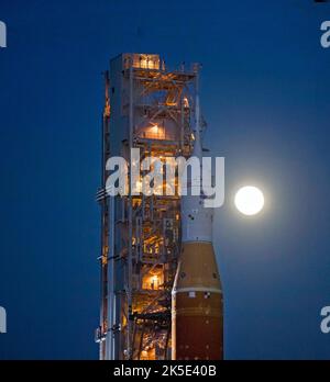 Der Mond steigt hinter der NASA-Rakete Space Launch System (SLS) mit der Orion-Sonde auf einem mobilen Trägerrakete auf, während er zum ersten Mal am 17. März 2022 im Kennedy Space Center der NASA in Florida, USA, zum Launch Complex 39B ausrollt. Im Vorfeld des Artemis I-Flugtests der NASA werden die vollständig gestapelte und integrierte SLS-Rakete und die Orion-Raumsonde im Launch Complex 39B einer Nassprobe unterzogen, um die Systeme zu verifizieren und Countdown-Verfahren für den ersten Start zu üben. Eine optimierte Version eines Originalbildes der NASA. Quelle: NASA/Agemignani Stockfoto