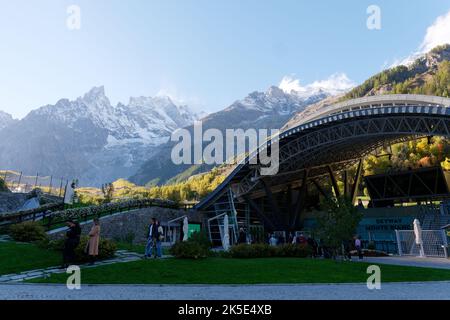 Seilbahnstation am unteren Ende des Skyway Monte Bianco Seilbahnsystems, Aosta Valley Italien. Die Touristen warten auf dem Grund mit Bergen dahinter. Stockfoto