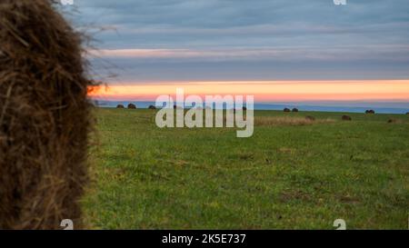 Gemähtes Feld mit unfokusstem Heuballen vor dem farbenfrohen Sonnenuntergang Stockfoto