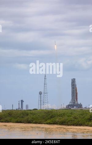 Eine SpaceX Falcon 9-Rakete, die einen Stapel der Starlink-Internet-Satelliten des Unternehmens trägt, hebt am 21. April 2022 vom Launch Complex 40 auf der Weltraumstation Cape Canaveral in Florida ab. Auf der rechten Seite sitzt die NASA-Rakete mit dem Raumschiff Orion auf einem mobilen Trägerrakete im Launch Complex 39B im Kennedy Space Center, während auf der linken Seite des Launch Complex 39A eine SpaceX Falcon 9-Rakete mit der Crew Dragon-Raumsonde des Unternehmens ist. Die Vorbereitungen für die Crew-4-Mission der Agentur zur Internationalen Raumstation dauern an. Stockfoto