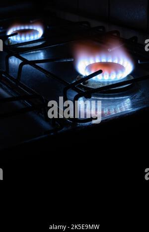 Gasherd zu Hause, natürliches Propangas brennt auf dunklem Hintergrund mit schwarzem Kopierraum, vertikale Ansicht der blauen Feuerflamme der Brenner. Konzept des Gases cos Stockfoto