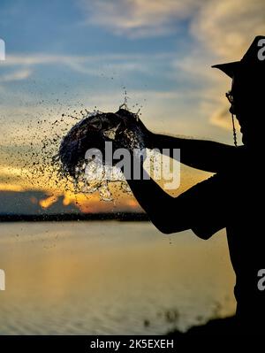 Ein Wasserballon platzt vor einem Sonnenuntergangshimmel. Stockfoto