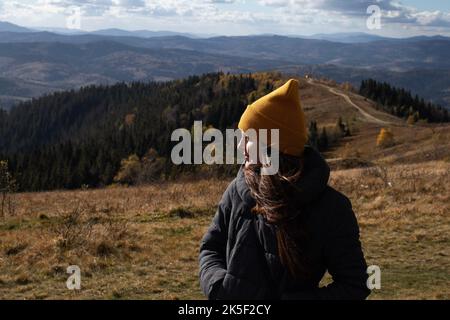 Junge glückliche Frau in oranger Mütze steht vor der Berglandschaft Stockfoto