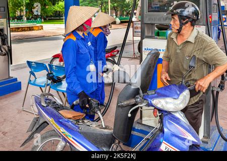 Tankstellenwärter mit Uniform und Bambushut zum Auffüllen des Motorrads, Hai Phong, Vietnam Stockfoto