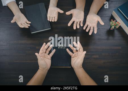 Eine Gruppe asiatischer Christen sitzt in einer katholischen Kirche und betet für den Segen Gottes, die blasse Sonne scheint am Ort der Anbetung. Stockfoto