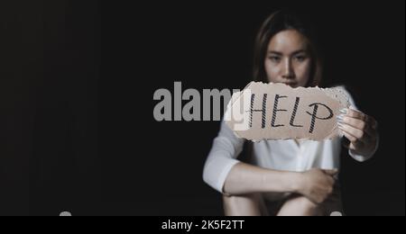 Frauen sitzen allein mit depressiver Expression und zeigen ein Papier mit einem Hilfetext. Schluss mit Gewalt gegen Frauen. Stockfoto