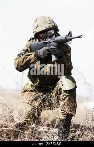 Warten und Beobachten. Ein Soldat hockte sich mit der Waffe in der Hand nieder und war bereit, in einer Wüstenumgebung zu feuern. Stockfoto