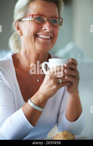 Einige wunderbare Gespräche während des Mittagessens. Eine hübsche ältere Frau schaut nachdenklich weg, während sie eine Tasse Kaffee genießt. Stockfoto