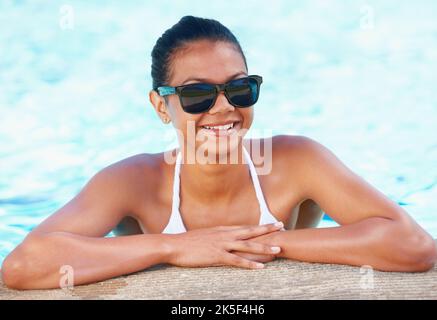 Sieht diesen Sommer gut aus. Beschnittene Ansicht einer jungen Frau in einem Swimmingpool, die lächelt und Schatten trägt. Stockfoto