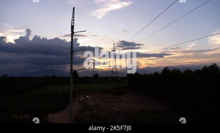 Silhouette eines elektrischen Stabes in der Dämmerung. Elektrische Pole und Drähte am Himmel bei Sonnenuntergang auf dem Land. Stockfoto