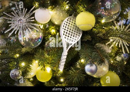 Dekorierter Weihnachtsbaum auf verschwommenem, glitzerndem und märchenhaftem Hintergrund. Ein Tennisschläger in Form eines Spielzeugs zur Dekoration eines Weihnachtsbaums für das Neue Stockfoto