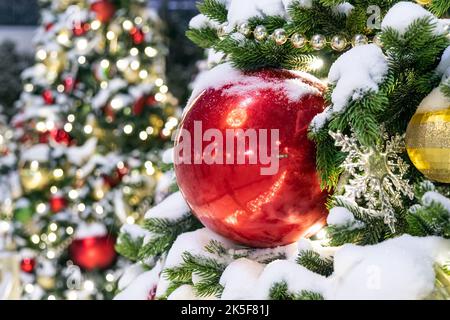 An einem sonnigen Wintertag steht im Park auf dem geschmolzenen Schnee ein eleganter Weihnachtsbaum, der mit roten und goldenen Luftballons geschmückt ist. Weihnachtskarte. Fichtenzweig Stockfoto