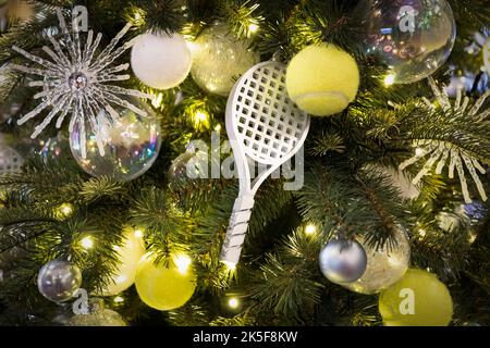 Dekorierter Weihnachtsbaum auf verschwommenem, glitzerndem und märchenhaftem Hintergrund. Ein Tennisschläger in Form eines Spielzeugs zur Dekoration eines Weihnachtsbaums für das Neue Stockfoto