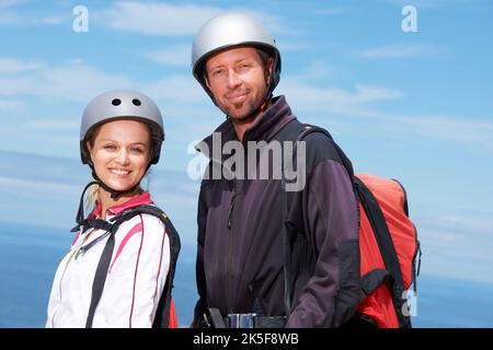 Sich vor ihrem Sprung aufgeregt fühlen. Zwei lächelnde Gleitschirme mit einem malerischen Blick im Hintergrund. Stockfoto