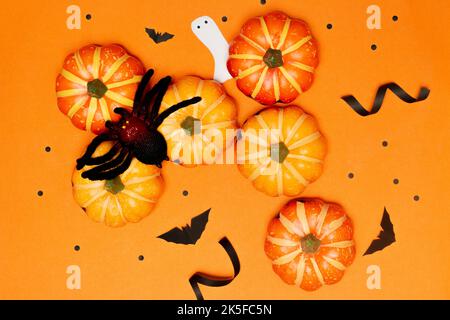 Halloween-Konzept, Spinne auf gruseligen Lächeln Kürbis und schwarze Fledermaus mit Geist auf orangefarbenem Hintergrund. Stockfoto