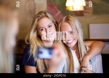 Lächeln Sie für die Kamera. Junge Freunde, die in einem Café fotografieren. Stockfoto