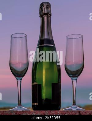 Eine Flasche Champagner mit zwei Flötengläsern daneben vor einem wunderschönen Sonnenuntergangshimmel Stockfoto