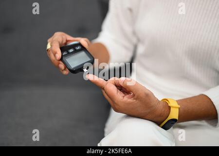 Reife Diabetikerin mit Blutzuckermessgerät am Finger, Messung des Blutzuckers. Diabetes und Gesundheitskonzept Stockfoto