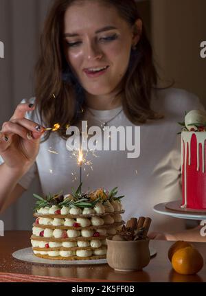 Kuchen und Wunderkerzen. Ein schönes, glückliches Mädchen zu Hause hält einen festlichen Neujahrskuchen auf einem Teller Stockfoto