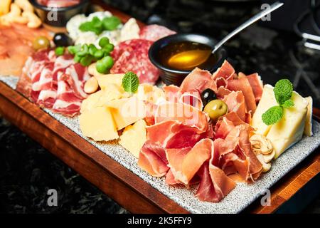 Ein Holzteller mit verschiedenen Käsesorten und geschnittenem, getrocknetem Feinkostfleisch Stockfoto