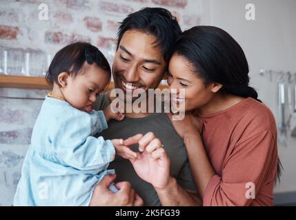 Familie mit Down-Syndrom-Baby, glückliche Eltern in Küche zu Hause zusammen und junge Kinderbetreuung. Indischer Vater hält niedliches Kind, asiatische Mutter lächeln mit Stockfoto