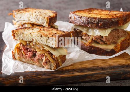 Klassisches Rindfleisch-Patty-Melt-Sandwich mit knusprigem Roggenbrot, Käse und zartem Zwiebel in der Nähe auf dem Holzbrett auf dem Tisch. Horizontal Stockfoto