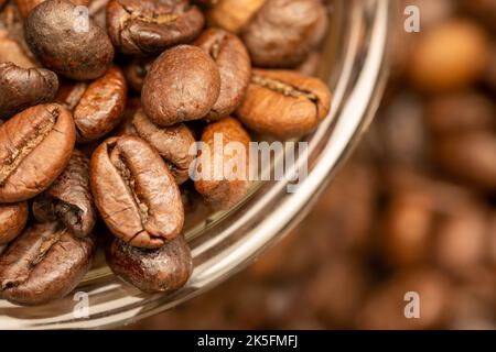 Geröstete Kaffeebohnen auf dem Tisch verstreut und eine kleine Kaffeetasse. Nahaufnahme, selektiver Fokus. Stockfoto