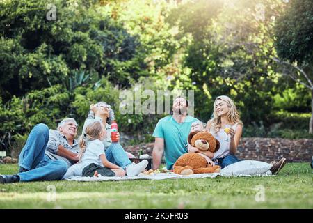 Glücklich, Natur und große Familie auf einem Picknick im Freien zusammen in einem grünen Garten blasen. Glück, ältere Großeltern und Eltern entspannen Stockfoto