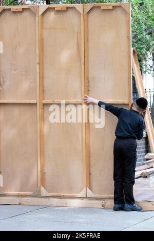 In Vorbereitung auf den Urlaub in Sukkos hilft ein orthodoxer jüdischer Junge seinem Vater, eine Sukkah zu bauen. In Williamsburg, Brooklyn, New York. Stockfoto