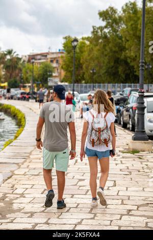 Ein junges Paar, Mann und Frau, die auf der griechischen Ferieninsel Zante oder zakynthos in griechenland entlang einer Meeresmauer am Meer spazieren. Stockfoto