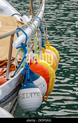 Eine Reihe farbenfroher pneumatischer Kunststoffkotflügel, die an der Seite eines Fischerboots hängen. Stockfoto