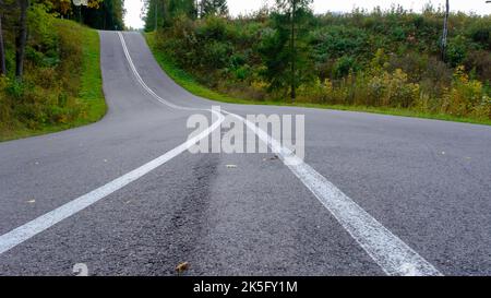 Asphaltierte Landstraße mit zwei weißen Streifen. Eine Kurve in der Straße mit einem Berg. Stockfoto