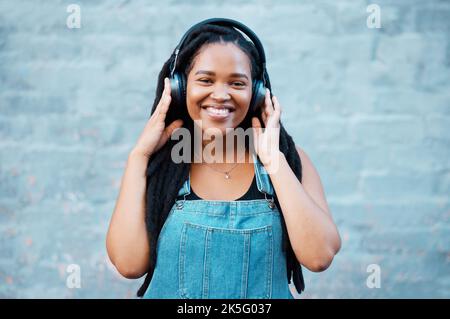 Gen z schwarze Frau, Musik-Kopfhörer und Porträt auf Wandhintergrund in Nigeria Stadt hören Radio, Audio und Sound. Glückliches junges afrikanisches Mädchen Stockfoto