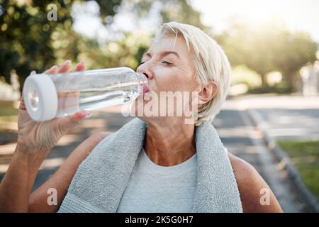 Ältere Fitness-Frau trinkende Wasserflasche im Freien nach dem Training, Laufen Training und Bewegung in der Nachbarschaft Straße. Durstige ältere Läuferin Stockfoto