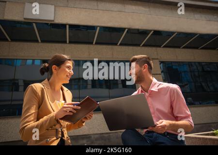 Ein junger talentierter Unternehmer arbeitet draußen in der Stadt, an einem sonnigen Tag, mit einem lustigen Gespräch Stockfoto