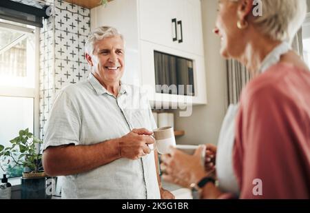 Älterer Mann, trinkt Kaffee und Gespräch mit einer Frau in der Küche zu Hause in Neuseeland. Glückliches, älteres und lächelndes Paar genießen Morgentee, plaudern und Stockfoto