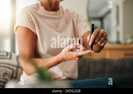 Gesundheitsfürsorge, Diabetes und eine ältere Frau, die Blutzuckertests an den Fingern im Wohnzimmer verwendet. Gesundheit, Innovation und Alltag der diabetischen Dame auf dem Sofa Stockfoto