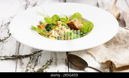 Lebensmittelbanner. Lachsschnitzel mit Fischbrühe und Gemüse. Appetitliche Fischfleischbällchen. Serviert auf einem weißen Teller. Weißer Hintergrund aus Holz. Speicherplatz kopieren Stockfoto