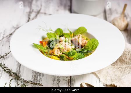 Lachsschnitzel mit Fischbrühe und Gemüse. Appetitliche Fischfleischbällchen. Serviert auf einem weißen Teller. Weißer Hintergrund aus Holz. Nahaufnahme Stockfoto