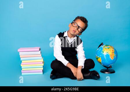 Ganzkörper-Foto von gesinnten kreativen Jungen sitzen Boden suchen interessiert leeren Raum auf blauem Hintergrund isoliert Stockfoto