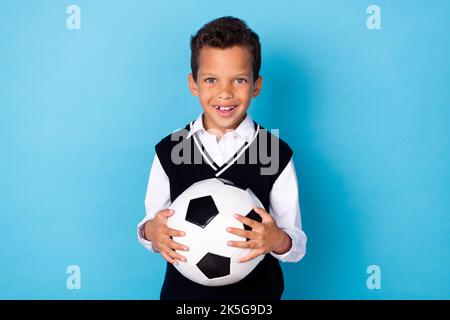 Portrait von fröhlich nett Schulkind Hände halten Fußball strahlend Lächeln isoliert auf blauem Hintergrund Stockfoto