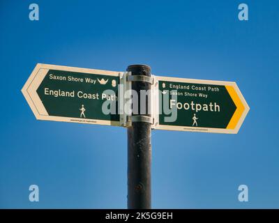 Zwei grüne Schilder auf einem grauen Metallpfosten weisen in die Richtungen des England Coast Path und des Saxon Shore Way. An einem sonnigen Tag im Sommer mit einem klaren, Stockfoto