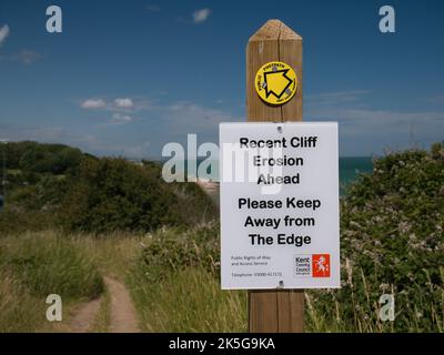 Ein weißes rechteckiges Schild, das an einem Holzpfosten neben einem Pfad befestigt ist, warnt Wanderer vor der jüngsten Erosion der Klippen am Küstenpfad. Aufgenommen an einem sonnigen Tag im Sommer Stockfoto