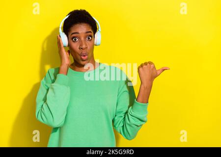 Foto von ziemlich beeindruckt androgynen menschlichen tragen grünen Pullover Ohrhörer zeigen leeren Raum isoliert gelben Hintergrund Stockfoto