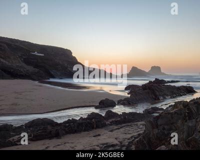 Nach Sonnenuntergang blaue Stunde Langzeitbelichtung Blick auf den Sandstrand Praia da Zambujeira do Mar mit Felsen und Klippen, kleinen Bach und mit verschwommenen Wellen im Ozean Stockfoto