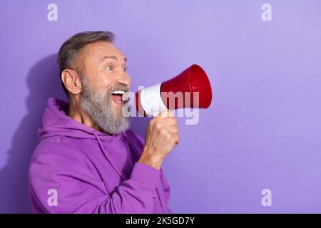 Foto eines Rentners mit weiß grauem Haar gekleidet lila Hoodie lautes Schreien in Megaphon isoliert auf violettem Hintergrund Stockfoto