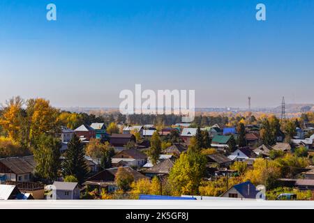 Luftaufnahme der traditionellen Holzhäuser, die den Zustand der Bevölkerung in der Nähe des Flusses Biya auf dem Hintergrund der Herbstlandschaft mit blauem Himmel zeigen. Chaotischer Betrug Stockfoto