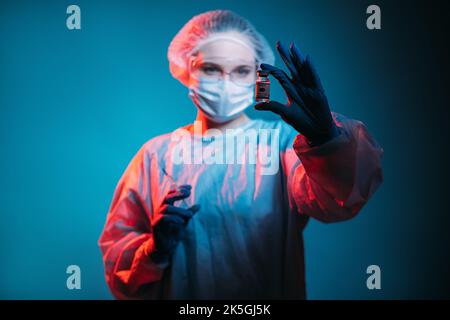 Impfstoffstudie. Coronavirus-Immunisierung. Laborforschung. Weibliche Wissenschaftlerin in ppe Gesichtsmaske Handschuhe Tests Dosis Fläschchen Flasche in roten Neonlicht-Isol Stockfoto