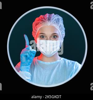Idee des Arztes. Lösung für das Gesundheitswesen. Ärztliche Beratung. Kopfbildnis einer elegant inspirierten Chirurgen in blauen ppe-Gesichtsmasken-Handschuhen mit Zeigefinger Stockfoto