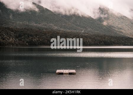 Luftaufnahme des ruhigen Sees mit gewelltem Wasser und einer kleinen hölzernen Plattform in der Mitte zwischen der Stille der bewaldeten einsamen Berge mit viel Stockfoto